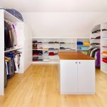 Offene, weiße Regale, an die Dachschräge angepasste Schränke und eine Wäscheinsel mit Holzdeckplatte