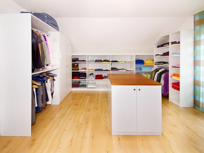 Offene, weiße Regale, an die Dachschräge angepasste Schränke und eine Wäscheinsel mit Holzdeckplatte