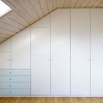 Individueller Einbauschrank als Kleiderschrank in der Dachschräge. Die Schubladen im niedrigen Bereich der Dachschräge sind mit lackiertem Glas belegt und setzen damit einen farblichen Akzent. Der Schrank ist perfekt eingebaut und zur Wand und zur Decke verblendet.