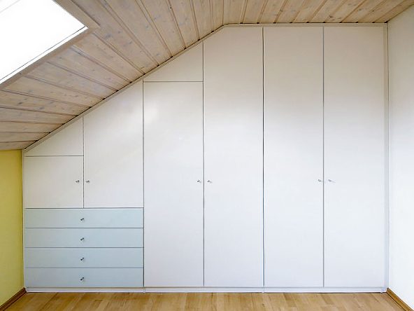 Individueller Einbauschrank als Kleiderschrank in der Dachschräge. Die Schubladen im niedrigen Bereich der Dachschräge sind mit lackiertem Glas belegt und setzen damit einen farblichen Akzent. Der Schrank ist perfekt eingebaut und zur Wand und zur Decke verblendet.