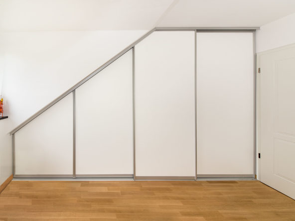 Schiebetürschrank in der Dachschräge in zeitlos modernem Design. Die Aluminiumrahmen und die weißen Türfüllungen sind optisch zurückhaltend. Der Schrank dient als Kleiderschrank in der Dachschräge.