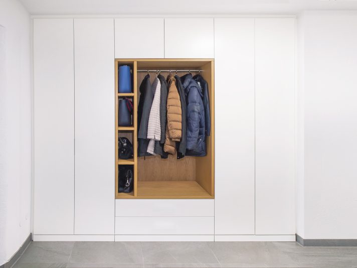 Komplett eingebauter, moderner Einbauschrank in Garderobe. Materialkombinkation aus Weißlack und Eiche. In der Mitte des Schrankes befindet sich eine offene Garderobennische. Die Fronten sind grifflos.