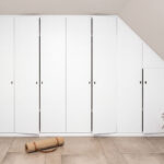 Weißer Schrank in der Dachschräge mit leicht geöffneten Türen. Das Bild wurde mit KI bearbeitet.