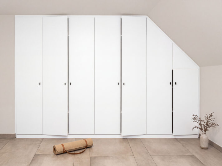 Weißer Schrank in der Dachschräge mit leicht geöffneten Türen. Das Bild wurde mit KI bearbeitet.