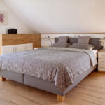 Zeitloser Schlafzimmer mit einem grauen Bett unter der Dachschräge. Bild wurde von KI retuschiert.