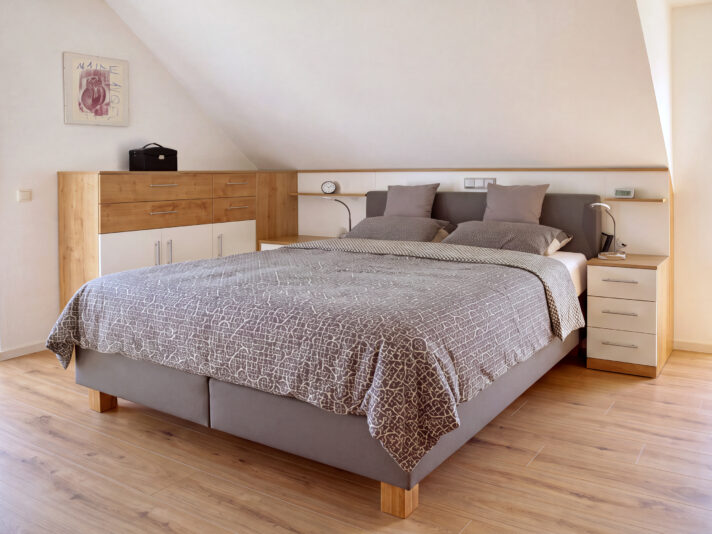 Zeitloser Schlafzimmer mit einem grauen Bett unter der Dachschräge. Bild wurde von KI retuschiert.