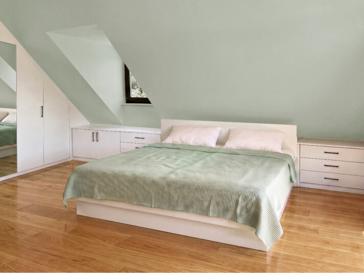 Dachschräge Schlafzimmer mit einem Doppelbett, mit weißen Kommoden und mit einem Einbauschrank einrichten. Bild von dieser Einrichtung wurde mit KI retouchiert.