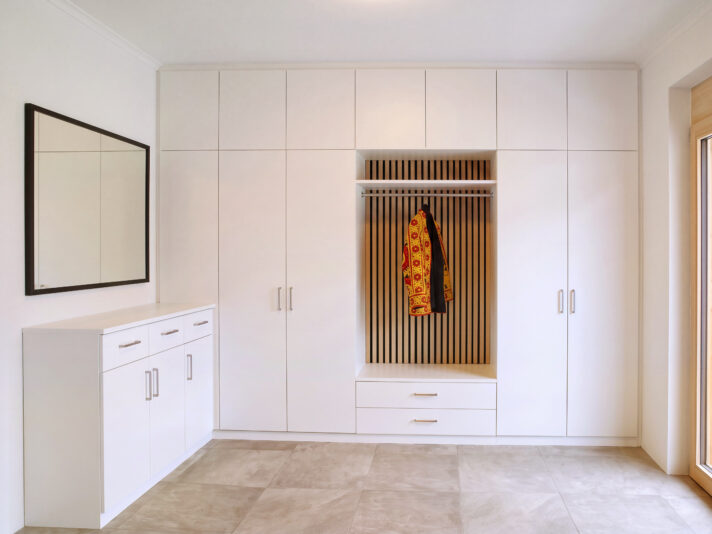 Großer, weißer Garderobenschrank mit einem Designpaneel, mit einer Ecklösung mit Kommode. Bild wurde von KI retuschiert.