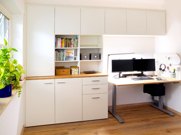 Homeoffice mit einem niedrig platzierten, höhenverstellbaren Schreibtisch, mit einem Tischüberbau, mit Schränken und mit weiß beschichteten Regalen einrichten. Bild wurde mit KI retuschiert.