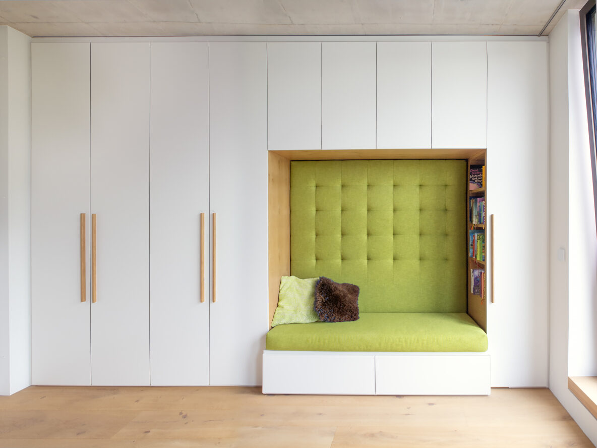 Weißer Schrank mit gepolsteter, grüner Sitznische. Lowboard mit Schublade, Hängeschränke.